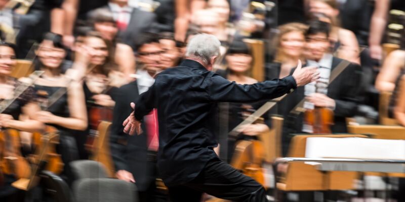 Rückansicht eines Dirigenten vor einem Orchester